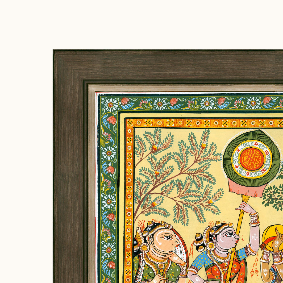 Close-up of a framed Indian folk art showing painted figures, a tree, and decorative borders, with a dark wood frame on a light background.