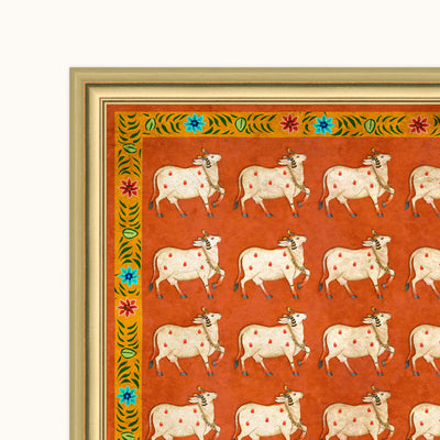 A framed art print featuring a repeating pattern of white cows with red spots on an orange background, bordered by a decorative green and blue floral frame.