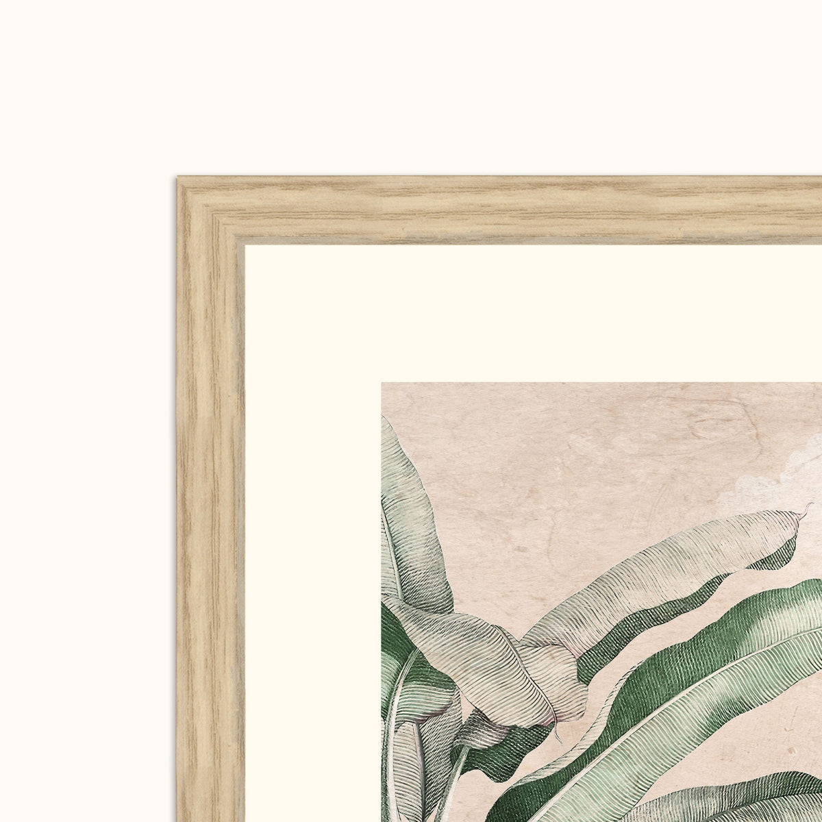 A close-up of a framed botanical art showing green illustrated leaves on a warm beige background, with a light wood frame and white mat against a white wall.