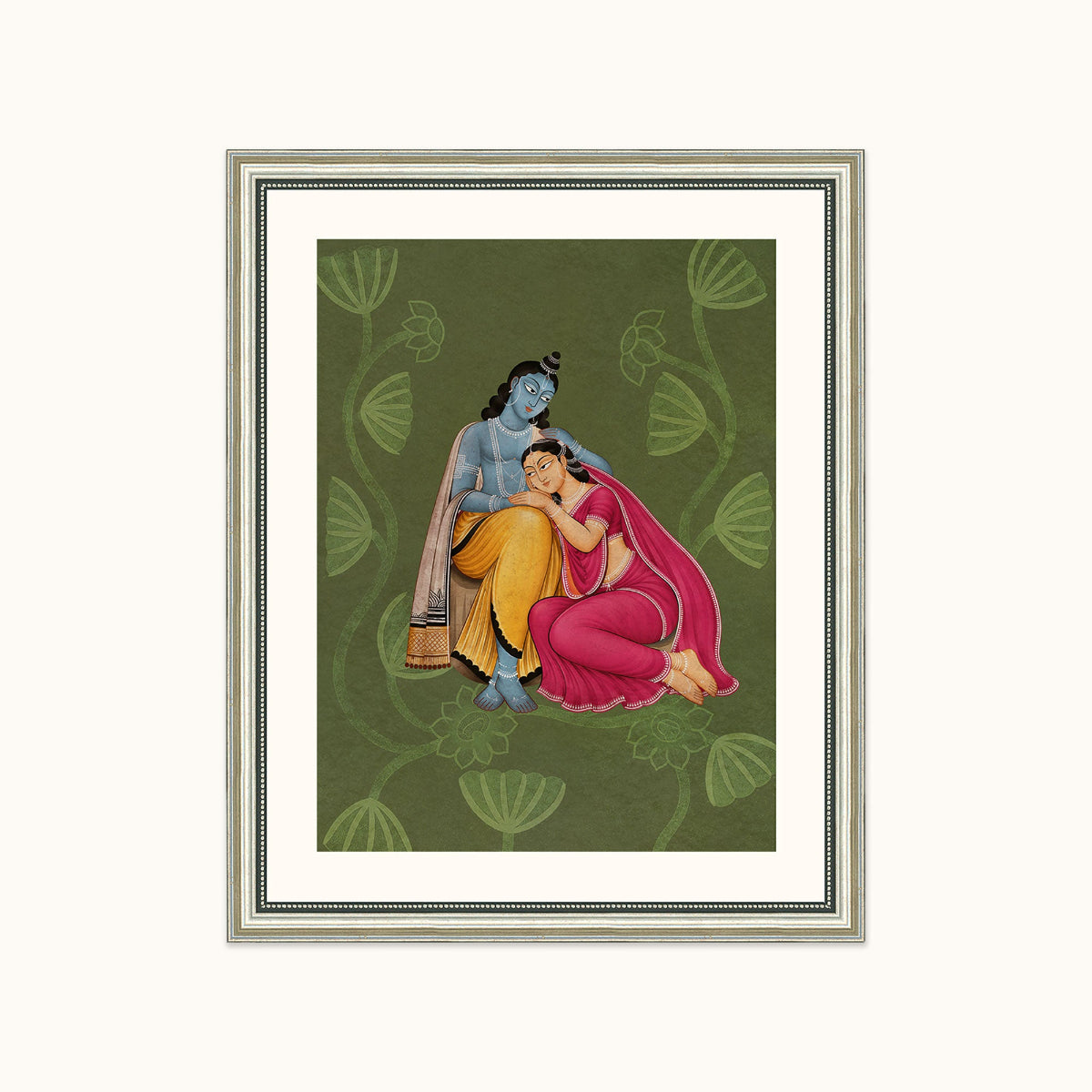 A framed art featuring a traditional Indian illustration of a blue-skinned krishna and a pink-skinned radhaji seated together on a dark green patterned background, shown against a light cream backdrop.
