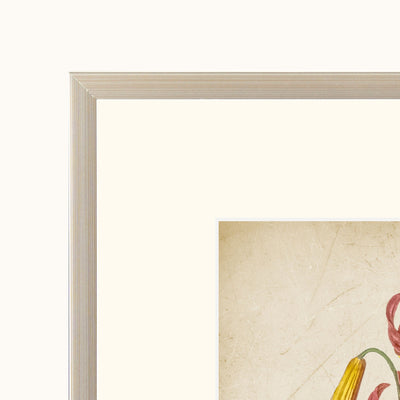 Close-up detail of a framed art showing a light beige wood frame, a wide cream mat, and a corner of the frame featuring a textured beige background with partial floral artwork in yellow, red, and green.